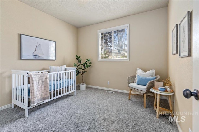 carpeted bedroom featuring a textured ceiling and a nursery area