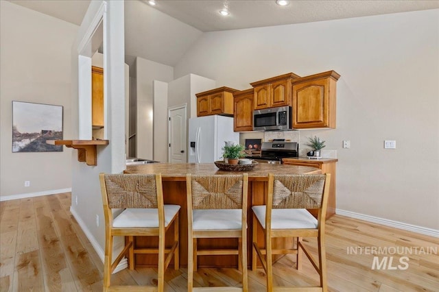 kitchen with appliances with stainless steel finishes, lofted ceiling, light hardwood / wood-style floors, and a breakfast bar area