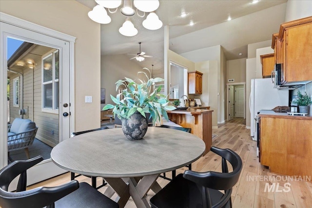 dining space with light wood-type flooring, ceiling fan with notable chandelier, vaulted ceiling, and sink