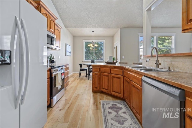 kitchen featuring appliances with stainless steel finishes, sink, light hardwood / wood-style flooring, a chandelier, and hanging light fixtures