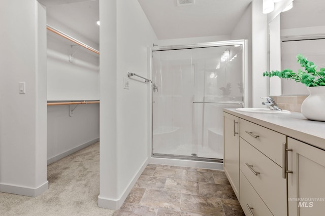 bathroom featuring baseboards, vanity, a spacious closet, and a shower stall