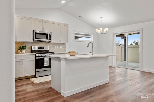 kitchen with decorative backsplash, appliances with stainless steel finishes, light countertops, a sink, and lofted ceiling