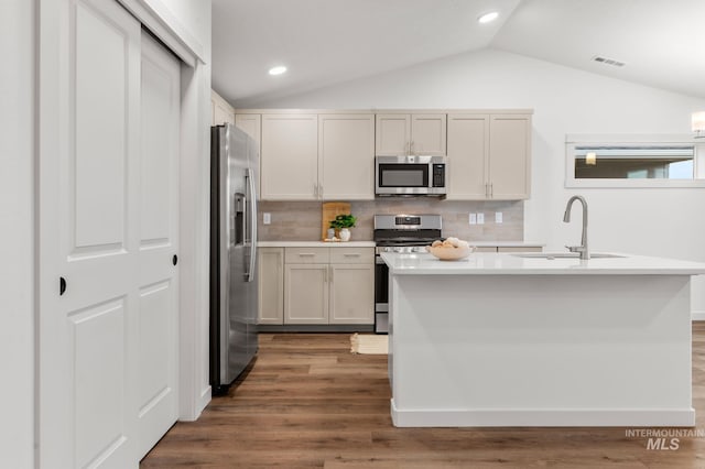 kitchen featuring appliances with stainless steel finishes, a sink, light countertops, wood finished floors, and lofted ceiling
