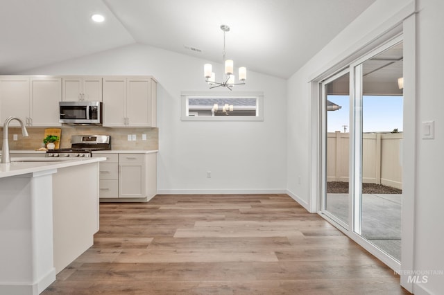 kitchen featuring a notable chandelier, appliances with stainless steel finishes, light countertops, tasteful backsplash, and vaulted ceiling