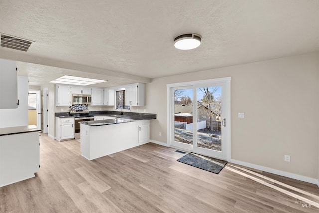 kitchen featuring stainless steel appliances, light hardwood / wood-style flooring, kitchen peninsula, a textured ceiling, and white cabinets