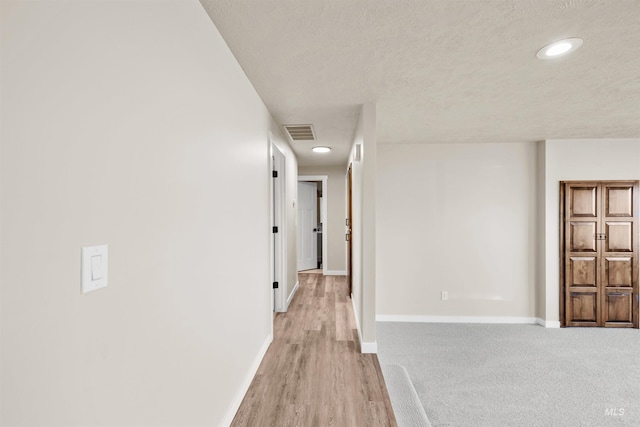 corridor with a textured ceiling and light hardwood / wood-style flooring