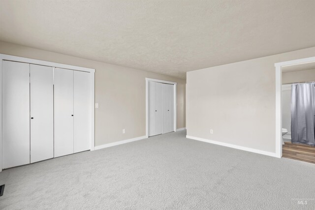 unfurnished bedroom featuring ensuite bathroom, carpet, and a textured ceiling