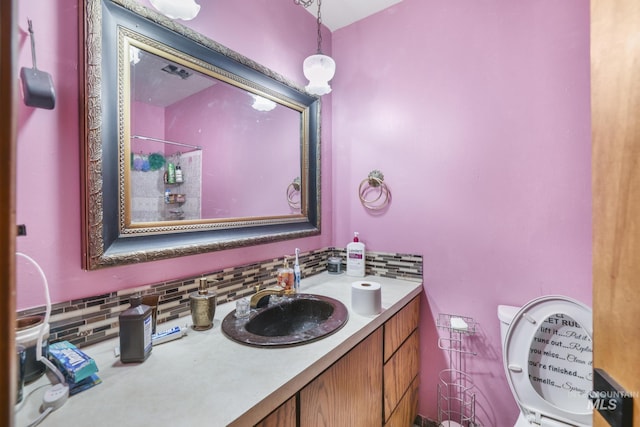 bathroom featuring vanity, toilet, a shower, and backsplash