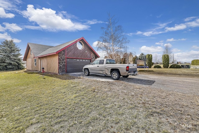 view of side of property featuring a lawn, an attached garage, gravel driveway, and a trampoline