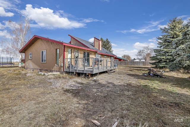 back of property featuring a deck, a trampoline, fence, and a chimney