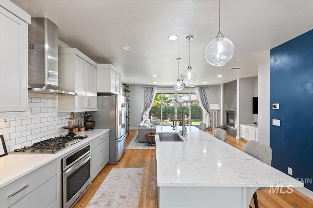 1765 E Bergeson St, Boise, ID 83706 - kitchen with stainless steel appliances, wall chimney range hood, light wood-style floors, open floor plan, and tasteful backsplash