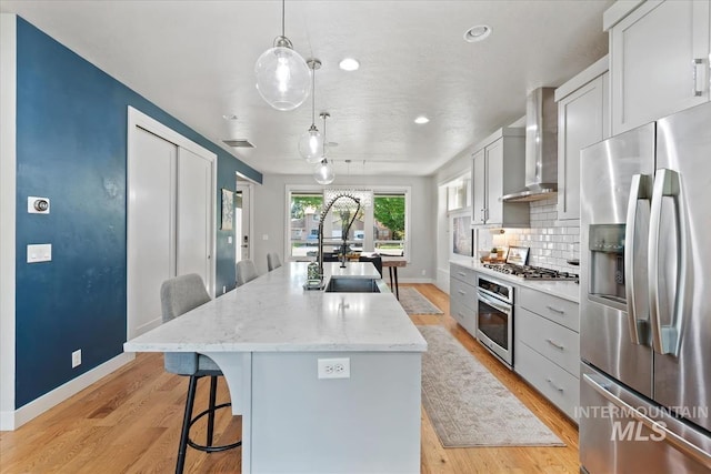 1765 E Bergeson St, Boise, ID 83706 - kitchen with stainless steel appliances, wall chimney range hood, baseboards, a sink, and an island with sink