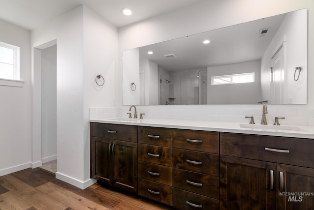 bathroom featuring vanity, hardwood / wood-style floors, a tile shower, and tasteful backsplash