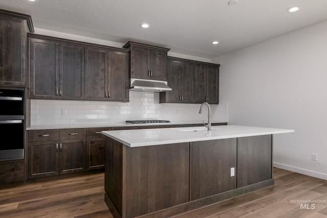 kitchen with sink, double oven, dark hardwood / wood-style flooring, and a center island with sink