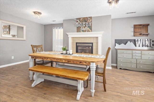 dining space featuring baseboards, visible vents, a tiled fireplace, and wood finished floors