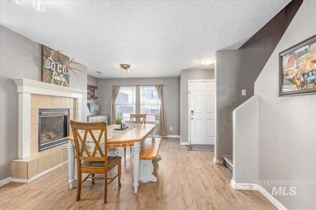 dining area with light wood finished floors, a textured ceiling, baseboards, and a tiled fireplace