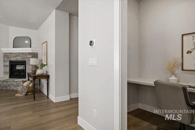 interior space featuring built in desk, a fireplace, baseboards, and wood finished floors