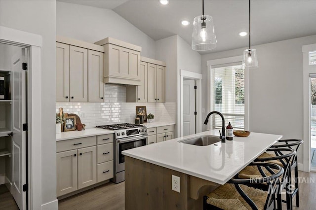 kitchen featuring wood finished floors, lofted ceiling, a sink, stainless steel gas range oven, and tasteful backsplash