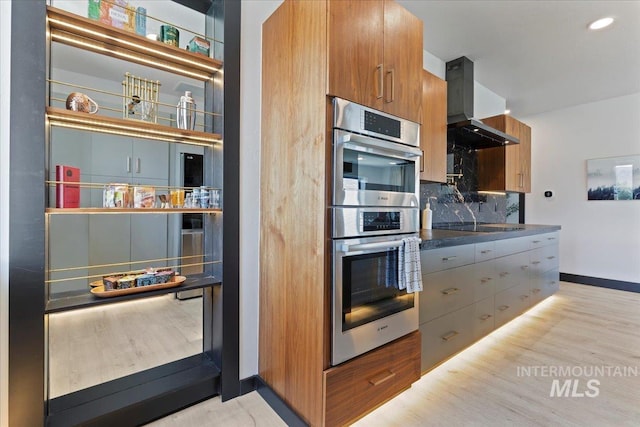15 Alder Creek Ln, Garden Valley, ID 83622 - kitchen featuring wall chimney exhaust hood, double oven, decorative backsplash, light wood-style flooring, and modern cabinets