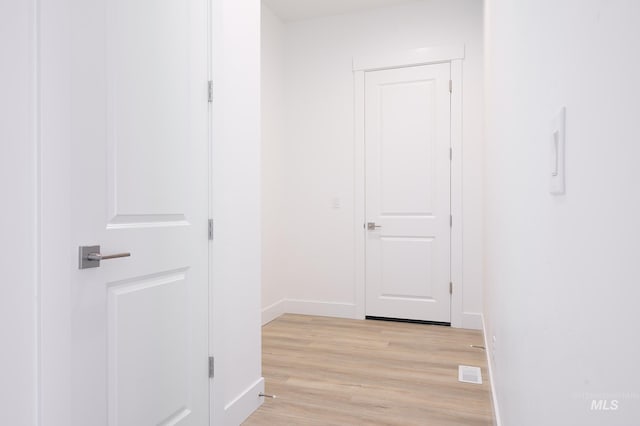 corridor with light wood finished floors, baseboards, and visible vents