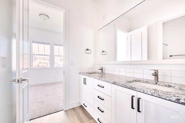 full bathroom featuring wood finished floors, double vanity, a sink, and decorative backsplash