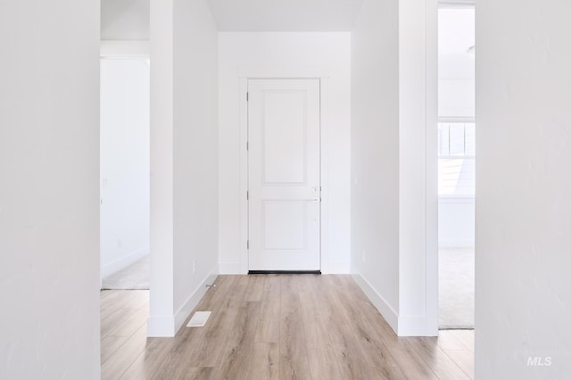 hall with light wood finished floors, baseboards, and visible vents