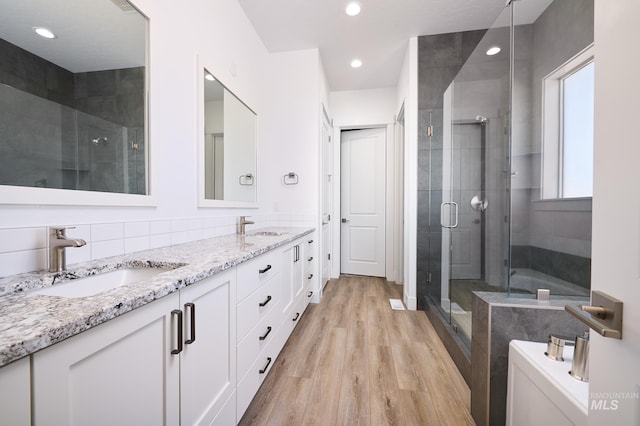 full bath featuring double vanity, a sink, a stall shower, and wood finished floors