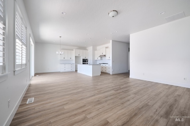 unfurnished living room with visible vents, baseboards, light wood finished floors, and a notable chandelier
