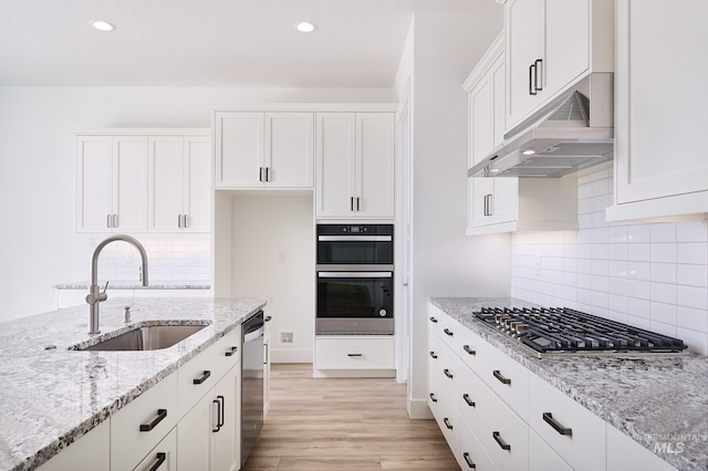 kitchen with a sink, light wood-style floors, under cabinet range hood, white cabinetry, and stainless steel appliances