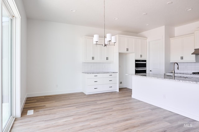 kitchen featuring white cabinets, an inviting chandelier, a sink, light wood finished floors, and light stone counters