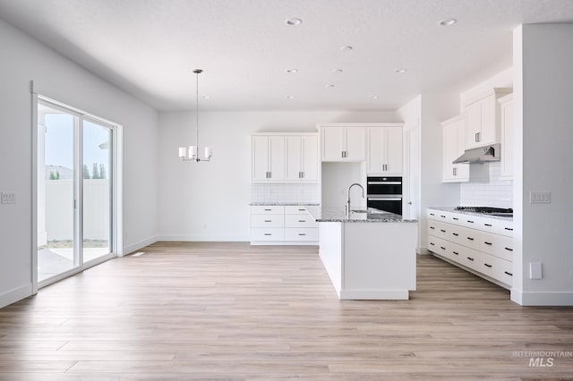 kitchen with a sink, light wood-style flooring, stone countertops, and under cabinet range hood