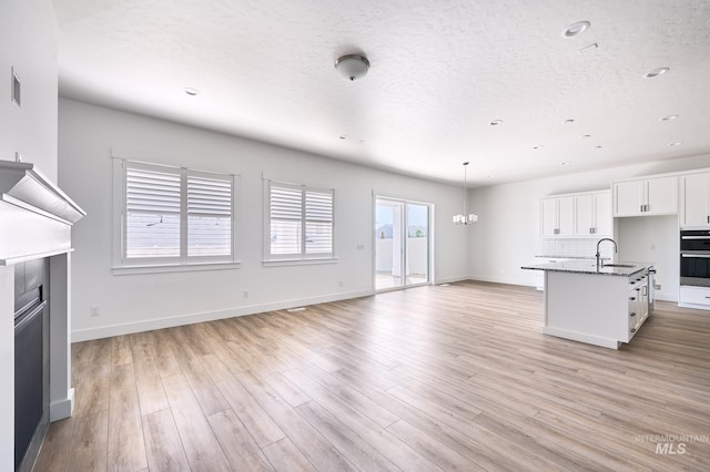 unfurnished living room featuring baseboards, a notable chandelier, a sink, a textured ceiling, and light wood finished floors