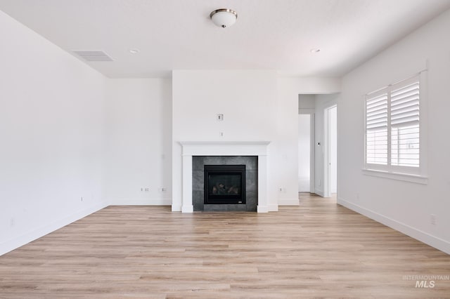 unfurnished living room with a fireplace, light wood finished floors, visible vents, and baseboards