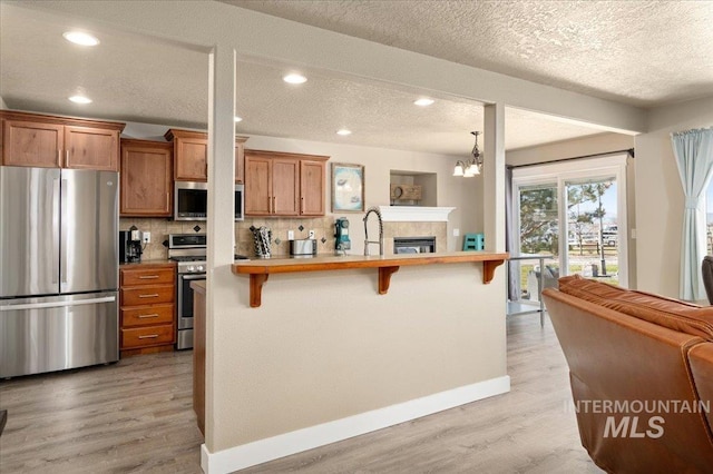 1375 Ross Rd, Weiser, ID 83672 - kitchen featuring appliances with stainless steel finishes, a kitchen breakfast bar, brown cabinets, light wood finished floors, and tasteful backsplash