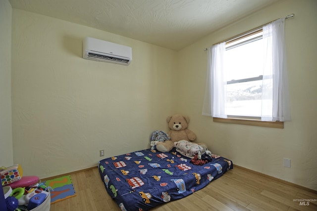 bedroom with a wall mounted air conditioner, a textured ceiling, and wood finished floors