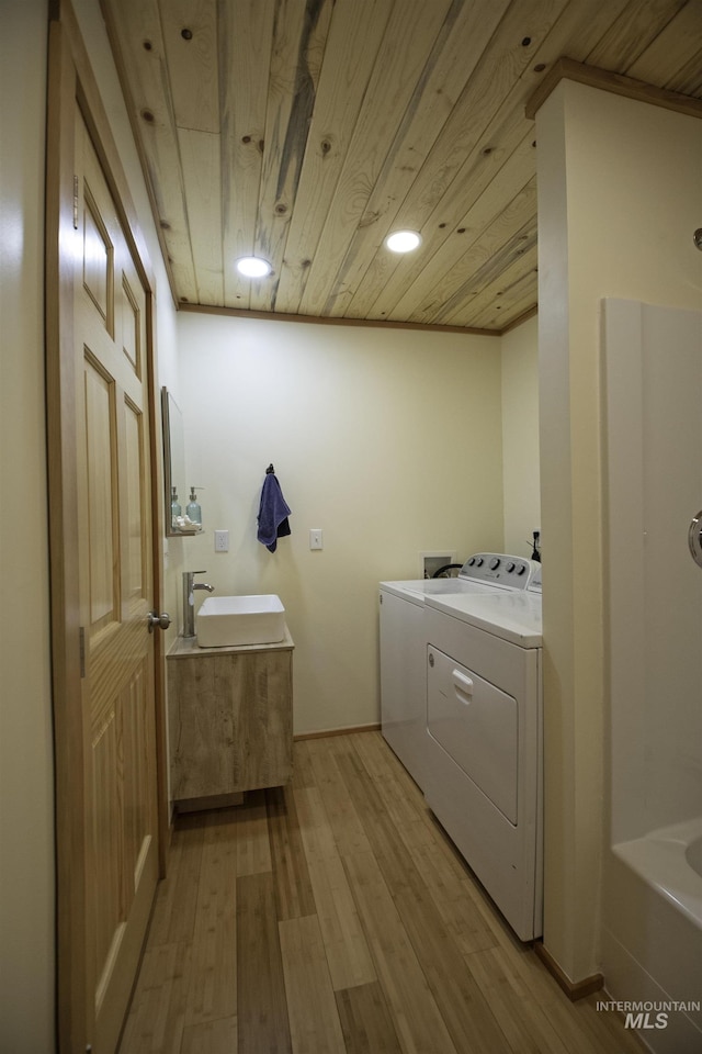 washroom with wooden ceiling, light wood-style floors, washing machine and dryer, a sink, and laundry area