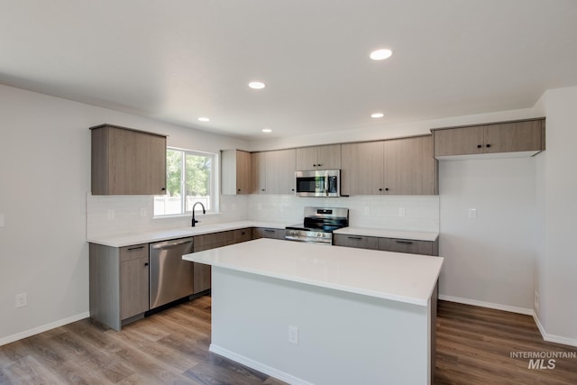 kitchen with light wood finished floors, stainless steel appliances, light countertops, a kitchen island, and a sink