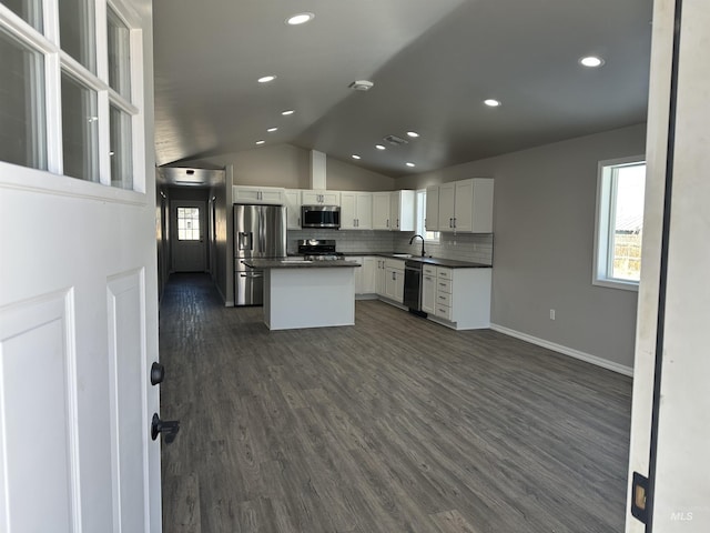 kitchen with dark wood finished floors, lofted ceiling, a sink, stainless steel appliances, and dark countertops