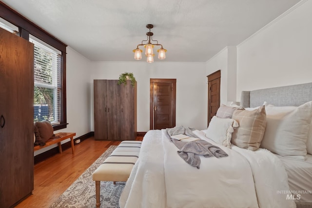 bedroom featuring light wood-type flooring, crown molding, baseboards, and a notable chandelier