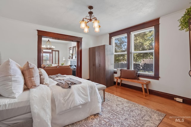 bedroom featuring baseboards, multiple windows, wood finished floors, and a notable chandelier