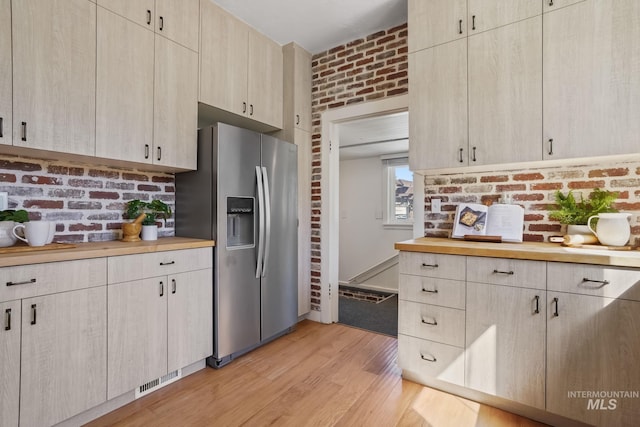 kitchen featuring brick wall, light wood-style floors, light brown cabinets, stainless steel refrigerator with ice dispenser, and wooden counters