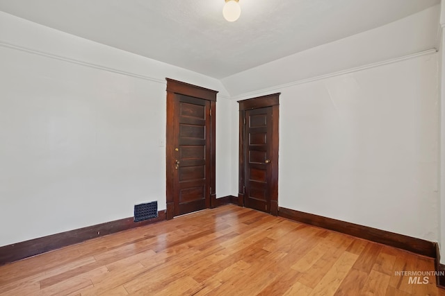 unfurnished room featuring lofted ceiling, light wood finished floors, visible vents, and baseboards