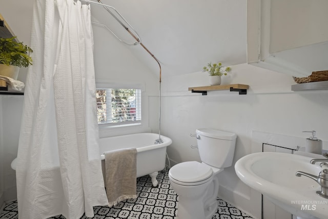 bathroom featuring a shower with shower curtain, toilet, lofted ceiling, a freestanding tub, and a sink