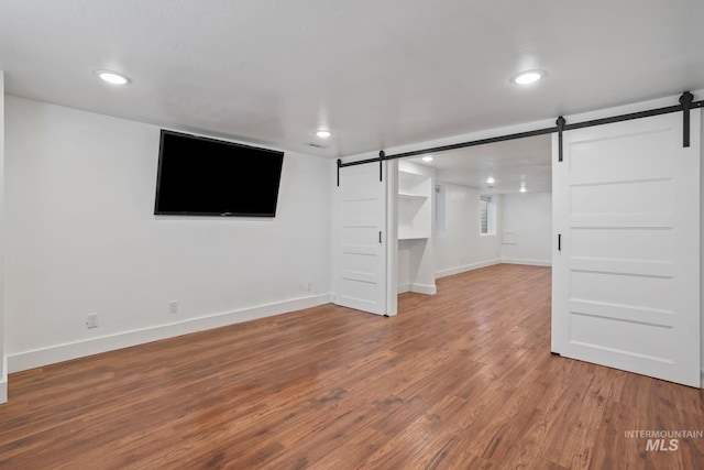 below grade area featuring a barn door, baseboards, wood finished floors, and recessed lighting