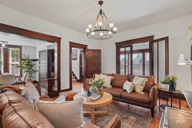 living room with a notable chandelier, light wood-style flooring, stairs, and crown molding