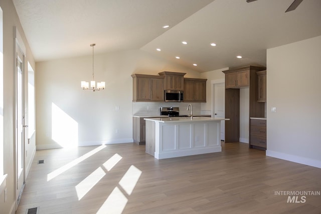 kitchen with an island with sink, light wood-style flooring, stainless steel appliances, and ceiling fan with notable chandelier