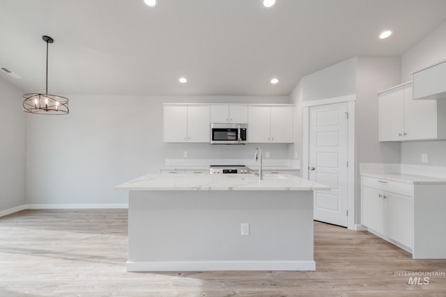 kitchen with white cabinetry, hanging light fixtures, light stone counters, a center island with sink, and light hardwood / wood-style flooring