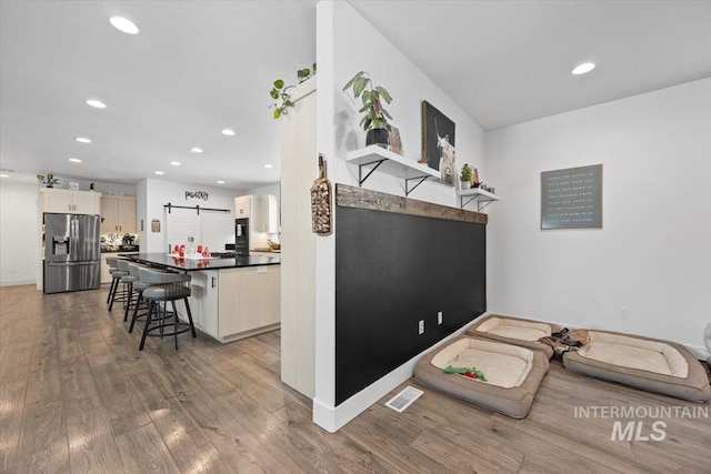 kitchen featuring a breakfast bar area, stainless steel fridge, kitchen peninsula, a barn door, and hardwood / wood-style floors