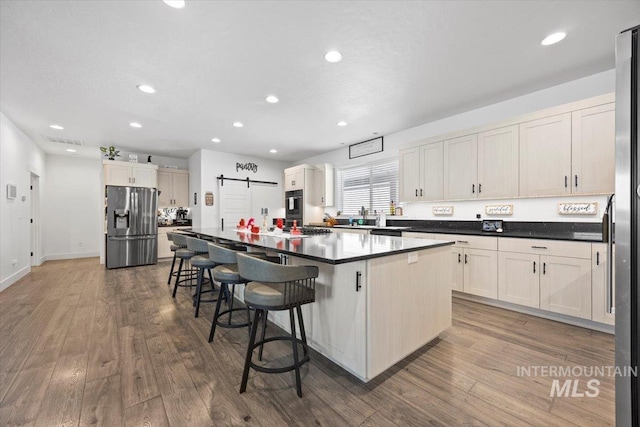 kitchen with a barn door, wood-type flooring, stainless steel fridge, and a center island