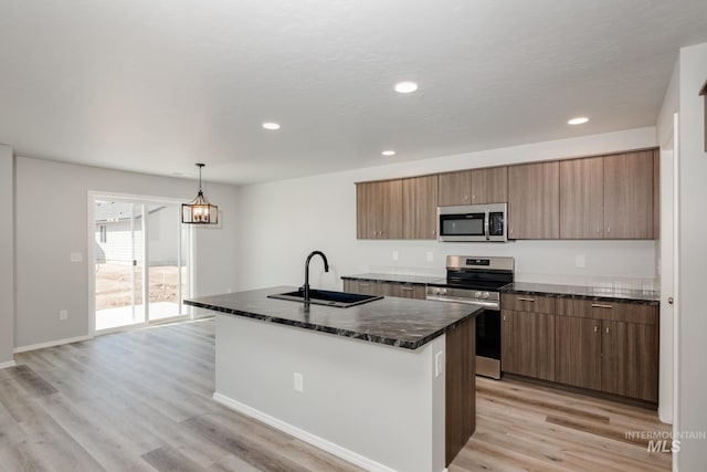 kitchen with a center island with sink, hanging light fixtures, sink, light wood-type flooring, and appliances with stainless steel finishes